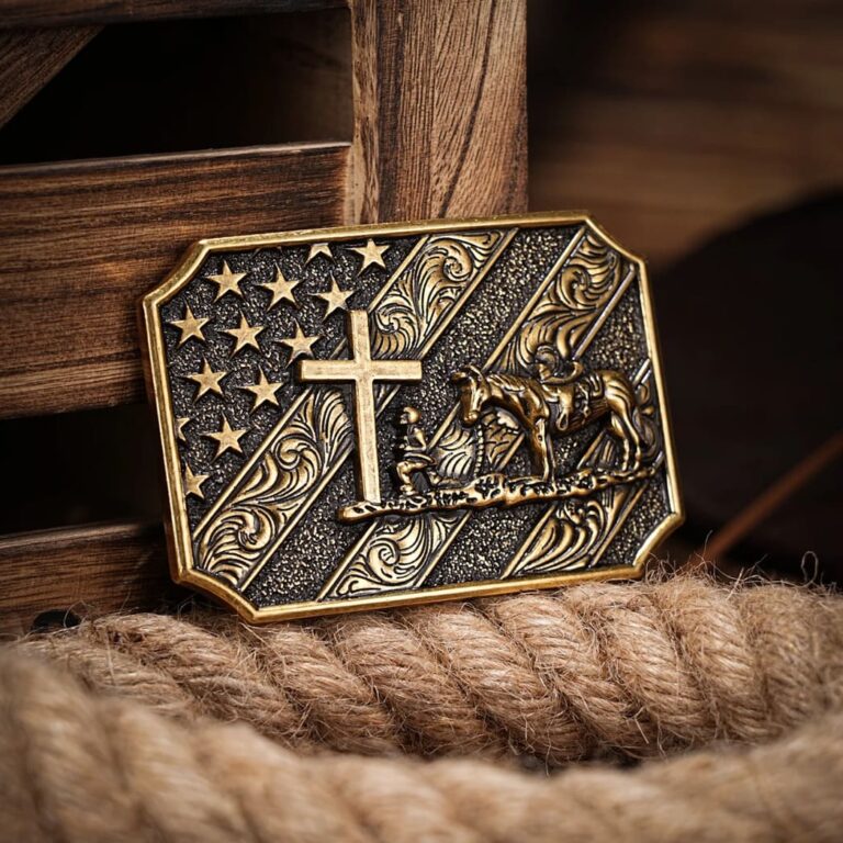 Bronze belt buckle featuring American flag, Christian cross, and praying cowboy with horse, embellished with scroll work designs.